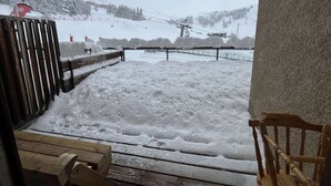 A snowy outdoor area with a wooden bench and a chair, a metal fence, and a ski lift in the background. - Modern studio at the foot of the slopes - 6 guests (Plagne Bellecôte)