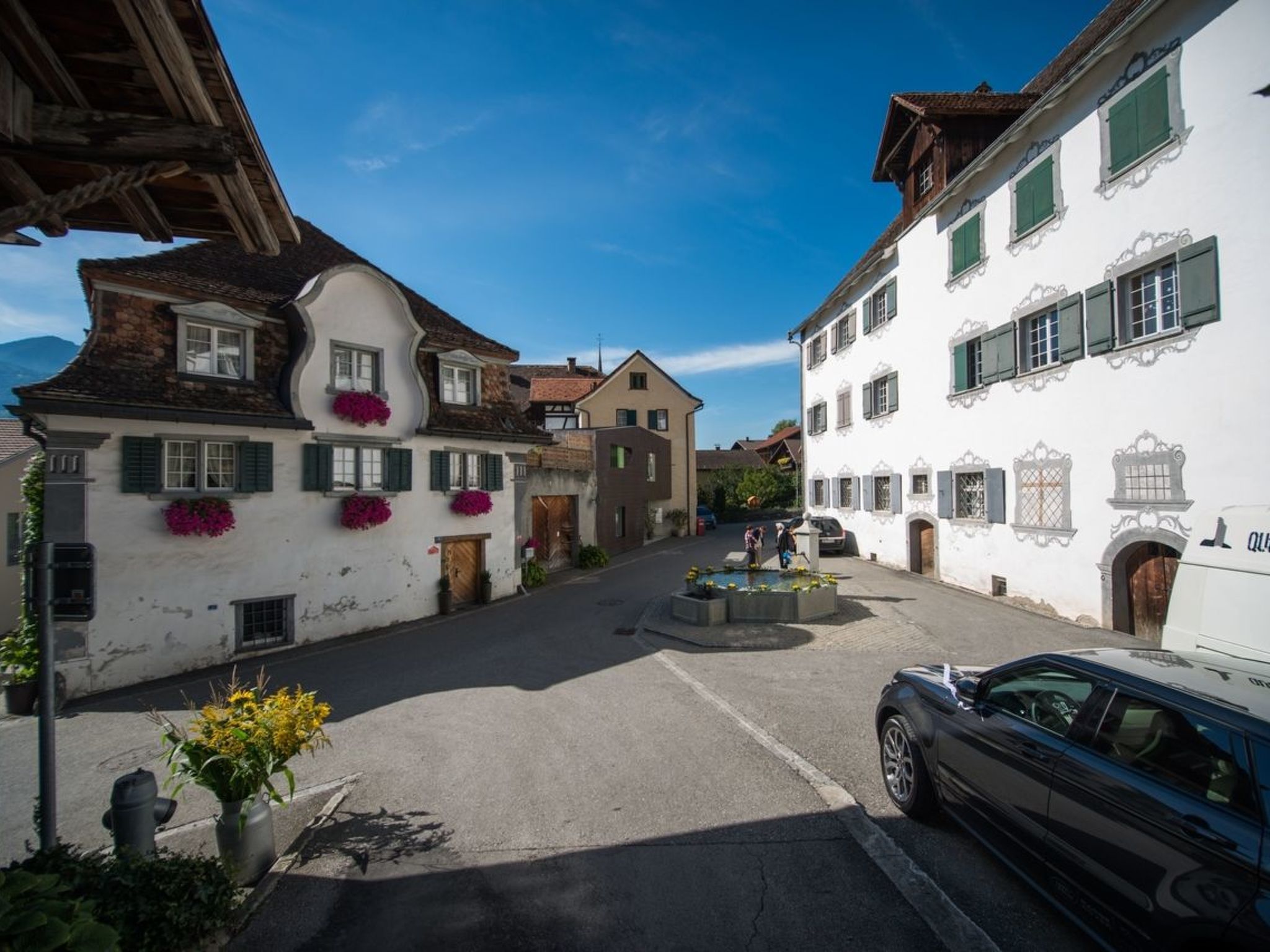 A narrow street with traditional buildings, a fountain, and a parked car.