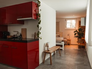 Een kleine keuken met rode kastjes, een houten bankje en een tafeltje.
