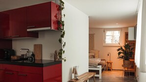 A compact kitchen with red cabinets, a wooden bench, and a small dining area with a table and chairs.