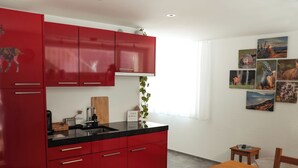 A modern kitchen with red cabinets, a black countertop, and a wooden dining table with chairs.
