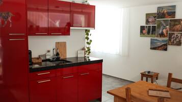 Une cuisine moderne avec des meubles de rangement rouges, un plan de travail noir et une table à manger en bois avec des chaises.