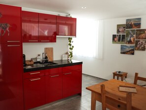 Une cuisine moderne avec des meubles de rangement rouges, un plan de travail noir et une table à manger en bois avec des chaises.