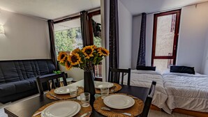 Una habitación moderna con una mesa de comedor preparada para dos personas, un sofá negro y una cama con ropa de cama blanca.