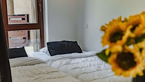 Habitación de hotel con dos camas, una ventana y un jarrón con girasoles.