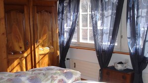A bedroom with a wooden wardrobe, a bed with floral bedding, and a window with patterned curtains. - Gäumann-Kiener, (Bad Ragaz), by Interhome (Bad Ragaz)