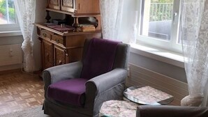 A room with a grey armchair, a small table, a wooden cabinet, and a window with curtains. - Gäumann-Kiener, (Bad Ragaz), by Interhome (Bad Ragaz)