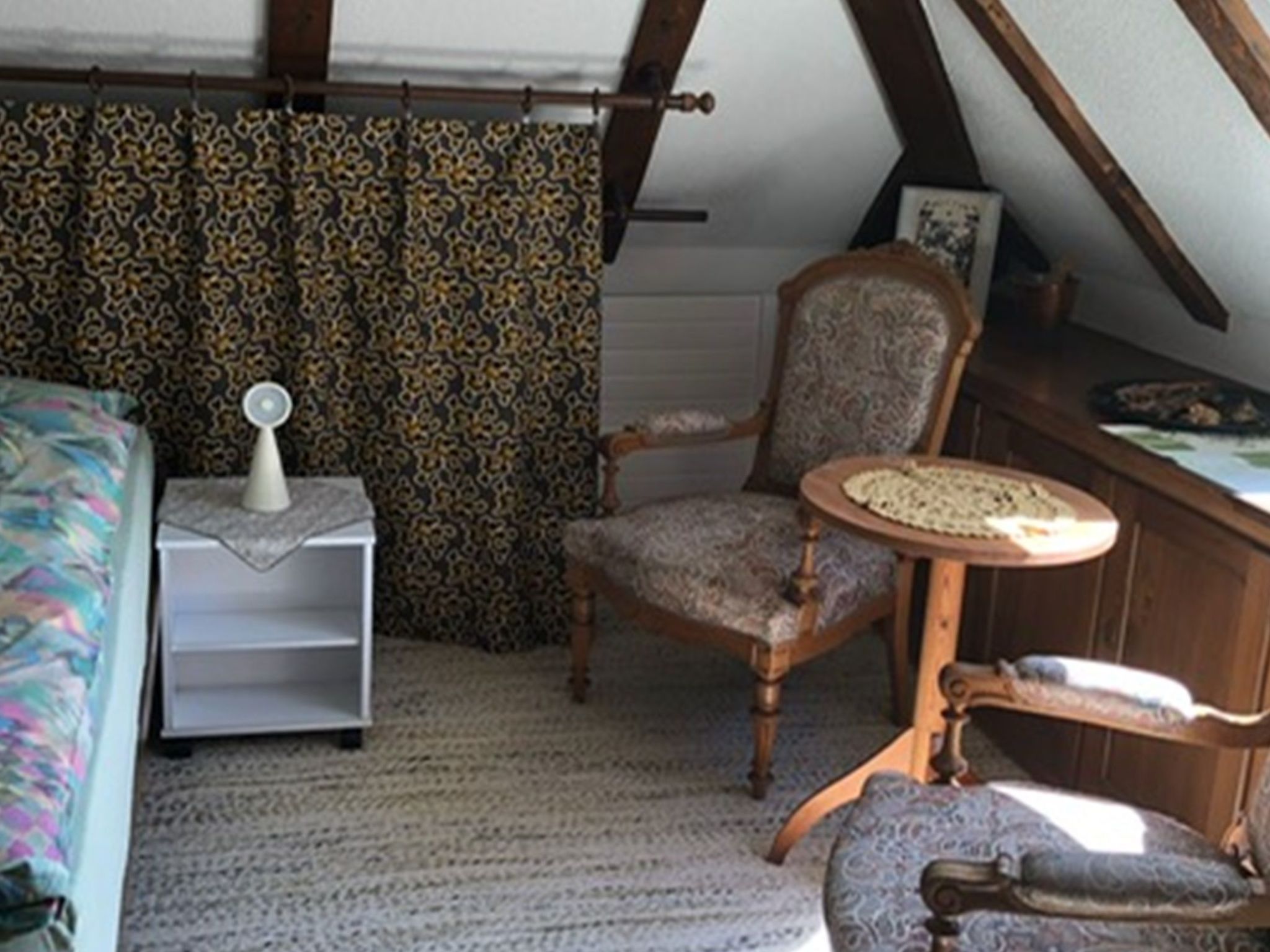 Une chambre à coucher avec un lit, une chaise, une petite table et une étagère.