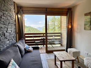 A cozy room with a sofa, a small table, and a view of a balcony with a wooden railing. - Modern apartment in Plagne Centre - 6 guests (La Plagne)