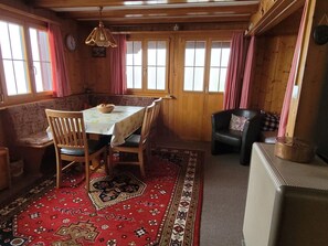 A cozy room with a wooden interior, a dining table with chairs, a sofa, a black leather chair, and a patterned rug.