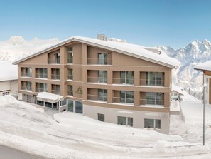 Ein mehrstöckiges Hotel mit Balkonen vor einer verschneiten Berglandschaft.