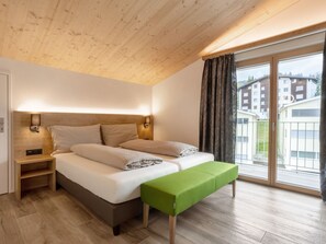 Ein Schlafzimmer mit einem Bett, Nachttischen, einer Bank und Blick auf Gebäude durch ein großes Fenster.