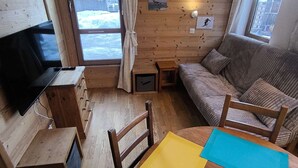 Una habitación acogedora con decoración de madera, televisión, sofá, mesita y ventana con vista a un paisaje nevado.