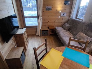 A cozy room with a wooden interior, a television, a sofa, a small table, and a window with a view of a snowy landscape. - Cozy studio, mountain view - 4 guests (Plagne Bellecôte)