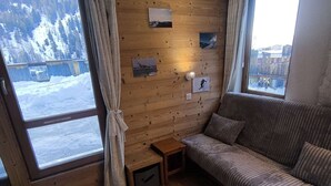 Una habitación acogedora con una pared de madera, un sofá, una mesita y una ventana con vistas a montañas nevadas.