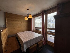 A wooden room with a bed, a bench, a wooden desk, a window with a view of a snowy landscape, and a hanging light fixture. - Cozy apartment mountain view - 10 guests (Belle Plagne)