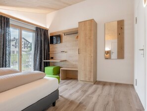 A modern bedroom with a bed, a TV, a wooden wardrobe, and a view of the outside. - Ferienwohnungen Tannenboden, (Flumserberg Tannenboden), by Interhome (Flumserberg Tannenheim)