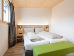 A bedroom with a bed, bedside tables, a nightstand, a green bench, and a window with curtains. - Ferienwohnungen Tannenboden, (Flumserberg Tannenboden), by Interhome (Flumserberg Tannenheim)