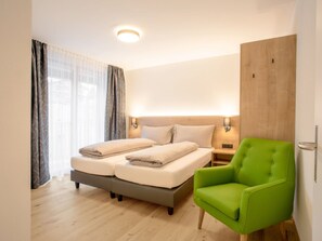 Une chambre d’hôtel avec un lit, un fauteuil vert, une armoire en bois et une table de chevet avec une lampe.