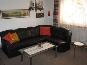 A black leather sofa with red and yellow cushions, a glass coffee table with a lace doily, a candle, and a small side table with a clock. - Frei, (Bad Ragaz), by Interhome (Bad Ragaz)