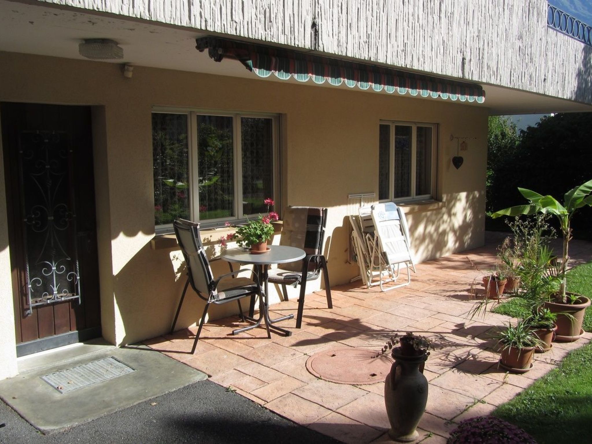 A patio with a table and chairs, a potted plant, and a door.