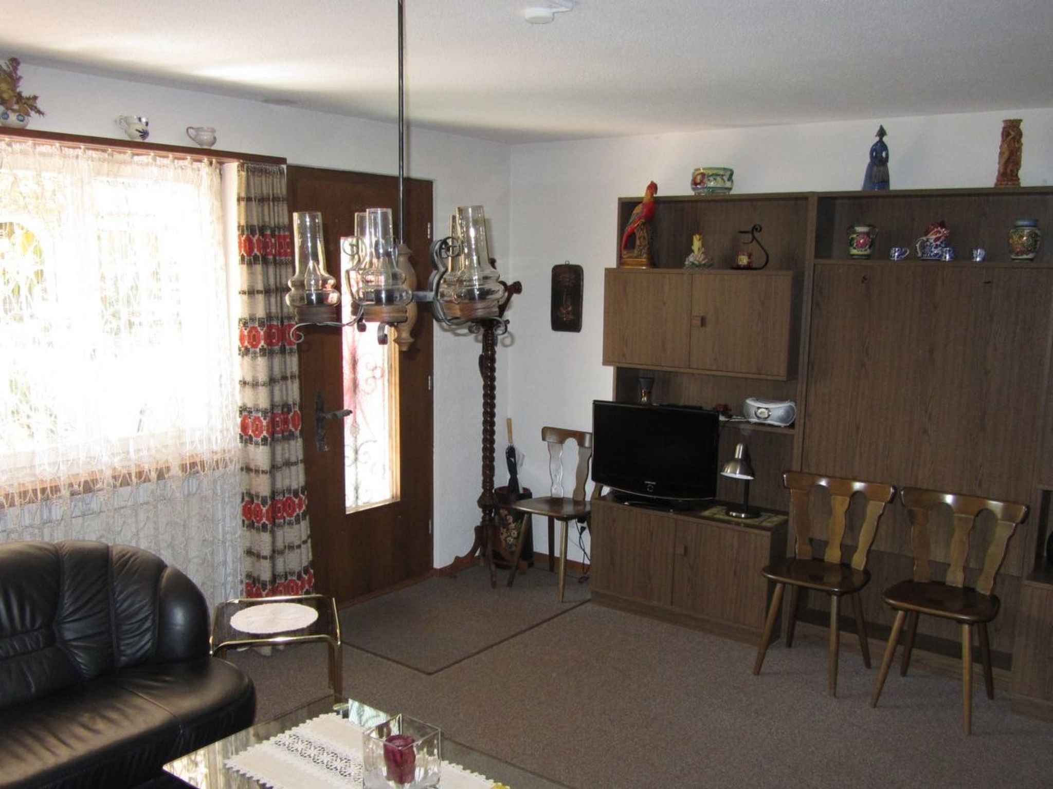 A living room with a black leather sofa, a glass coffee table, a television, and wooden chairs.