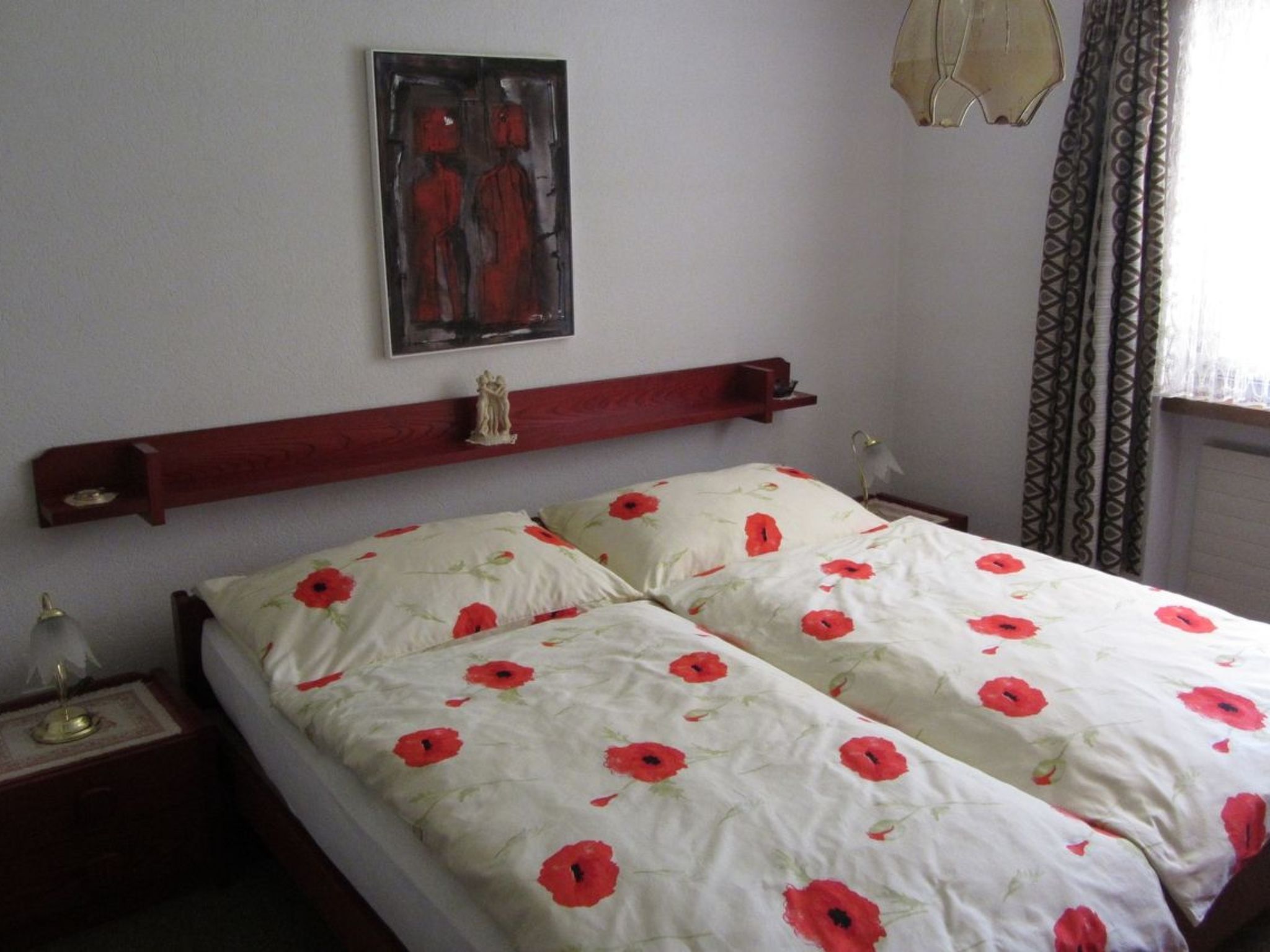 A bedroom with a bed, a nightstand, a wall-mounted shelf, and a painting.