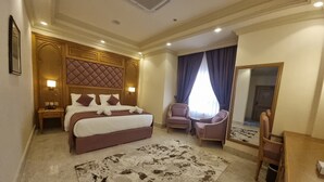 Habitación de hotel con una cama grande, una zona de estar con una silla y una mesa, un espejo y una alfombra.