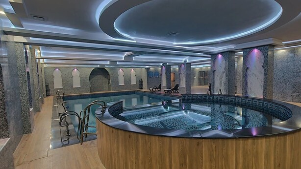Un espacio de spa moderno con un jacuzzi central, suelo de madera y paredes de piedra.
