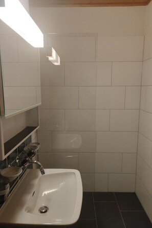 Un baño con lavamanos blanco, espejo y zona de ducha.