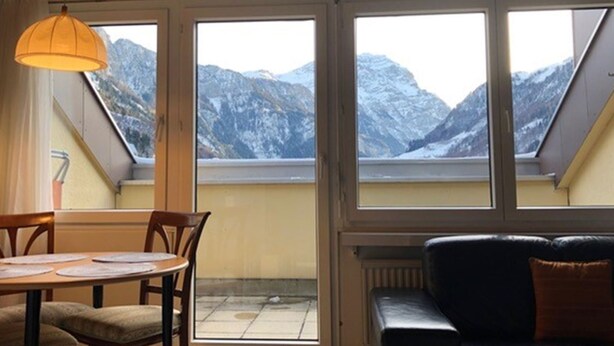 Una habitación con una mesa y sillas, un sofá de cuero negro y ventanas amplias con vistas a la montaña.