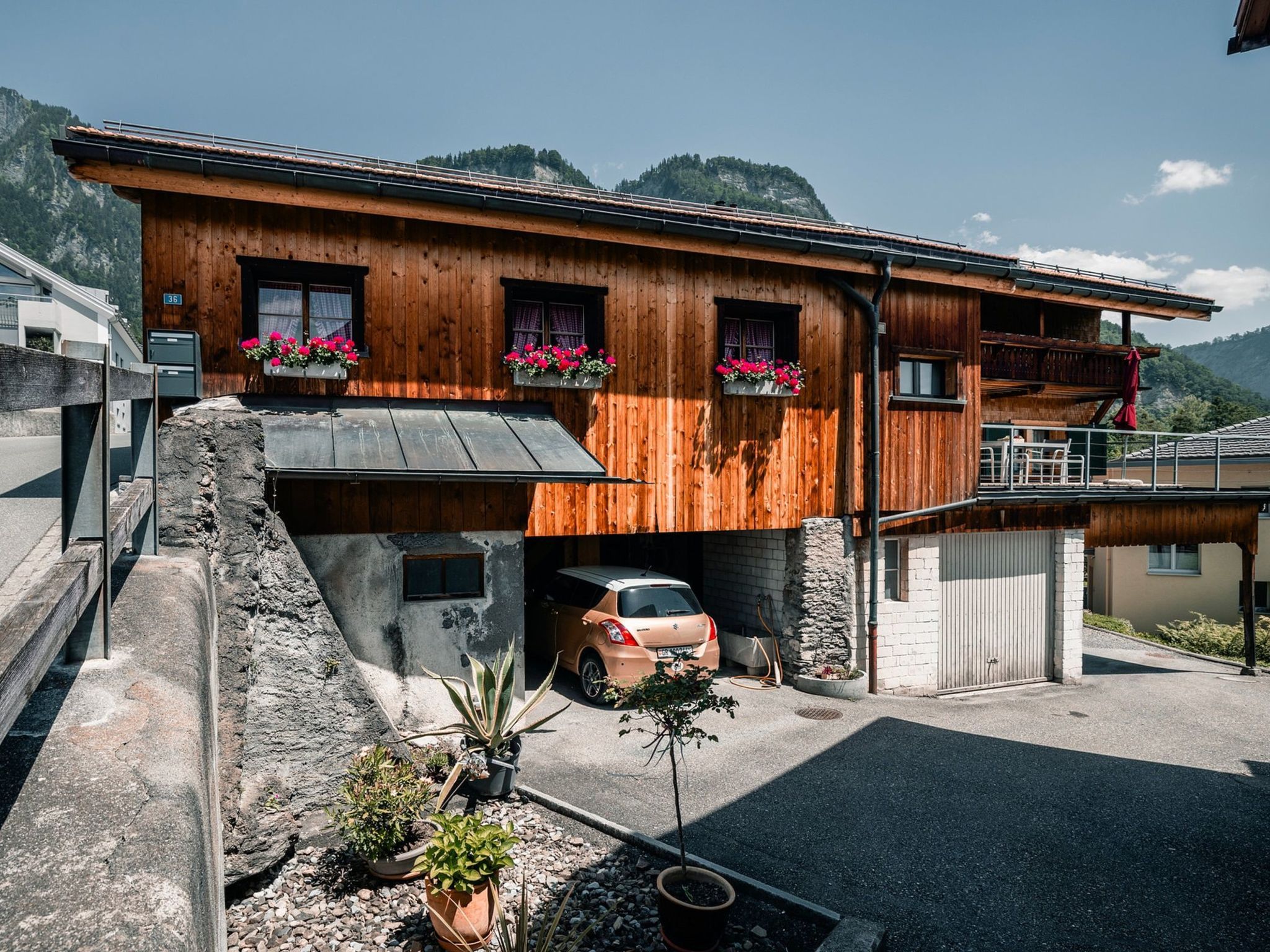 Uma casa de madeira com um carro estacionado na entrada, rodeada por vasos de plantas.