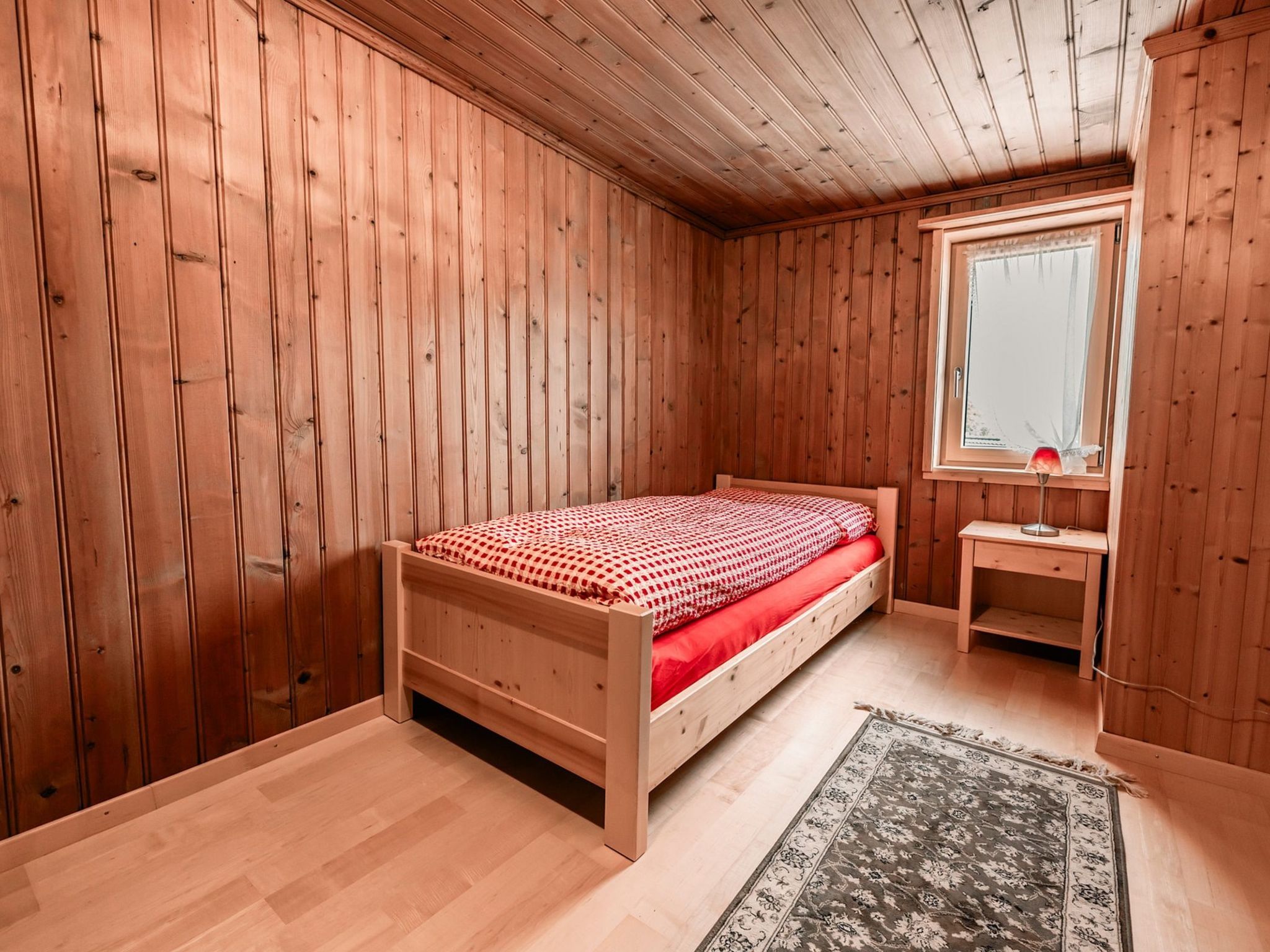 Ein Zimmer mit Holzboden, einem Bett, einem Schreibtisch und einem Fenster.