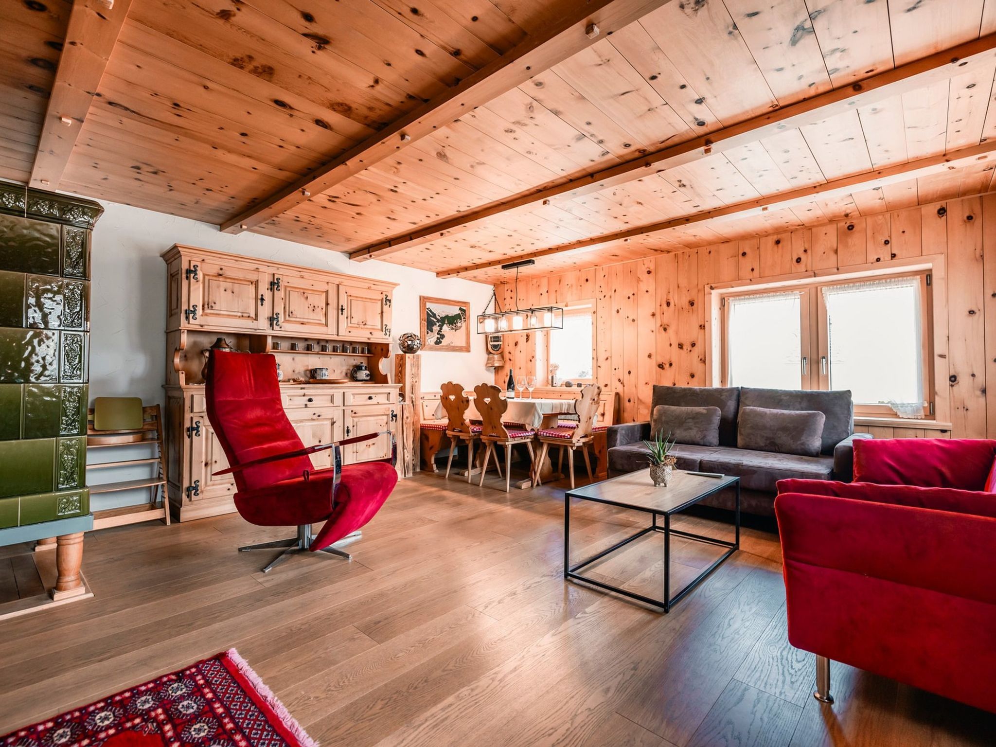 A wooden interior with a dining area, sofa, and red armchair.