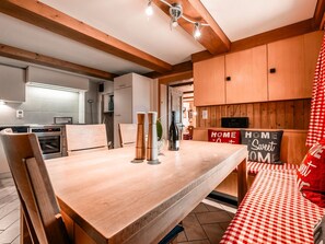 A wooden dining table with chairs, a kitchen area with cabinets, and a red and white checkered tablecloth.