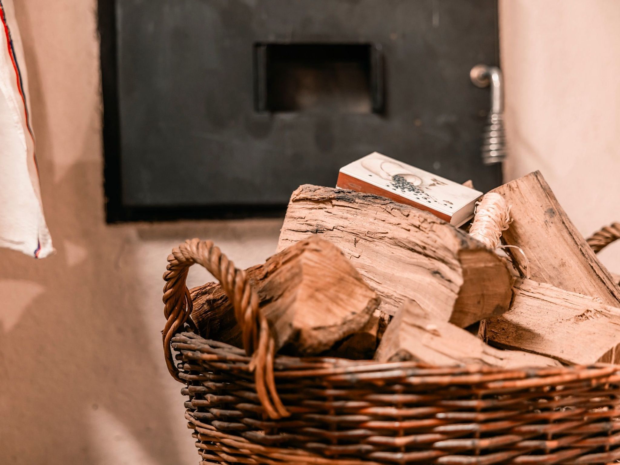Ein Korbkörbchen mit Holzscheiten und einem Buch, an eine Wand mit einer Tür gelehnt.