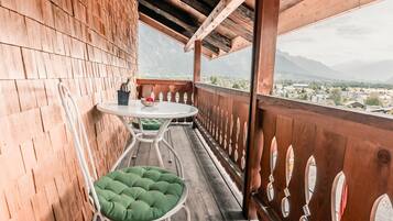 A wooden balcony with a table and chairs, overlooking a mountainous landscape.