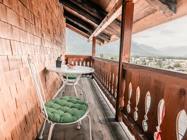 A wooden balcony with a table and chairs, overlooking a mountainous landscape.