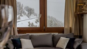 Un soggiorno con divano, una finestra vista su un paesaggio innevato e una porta in legno.