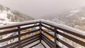 Paesaggio montuoso innevato con vista su edifici e una recinzione in legno.