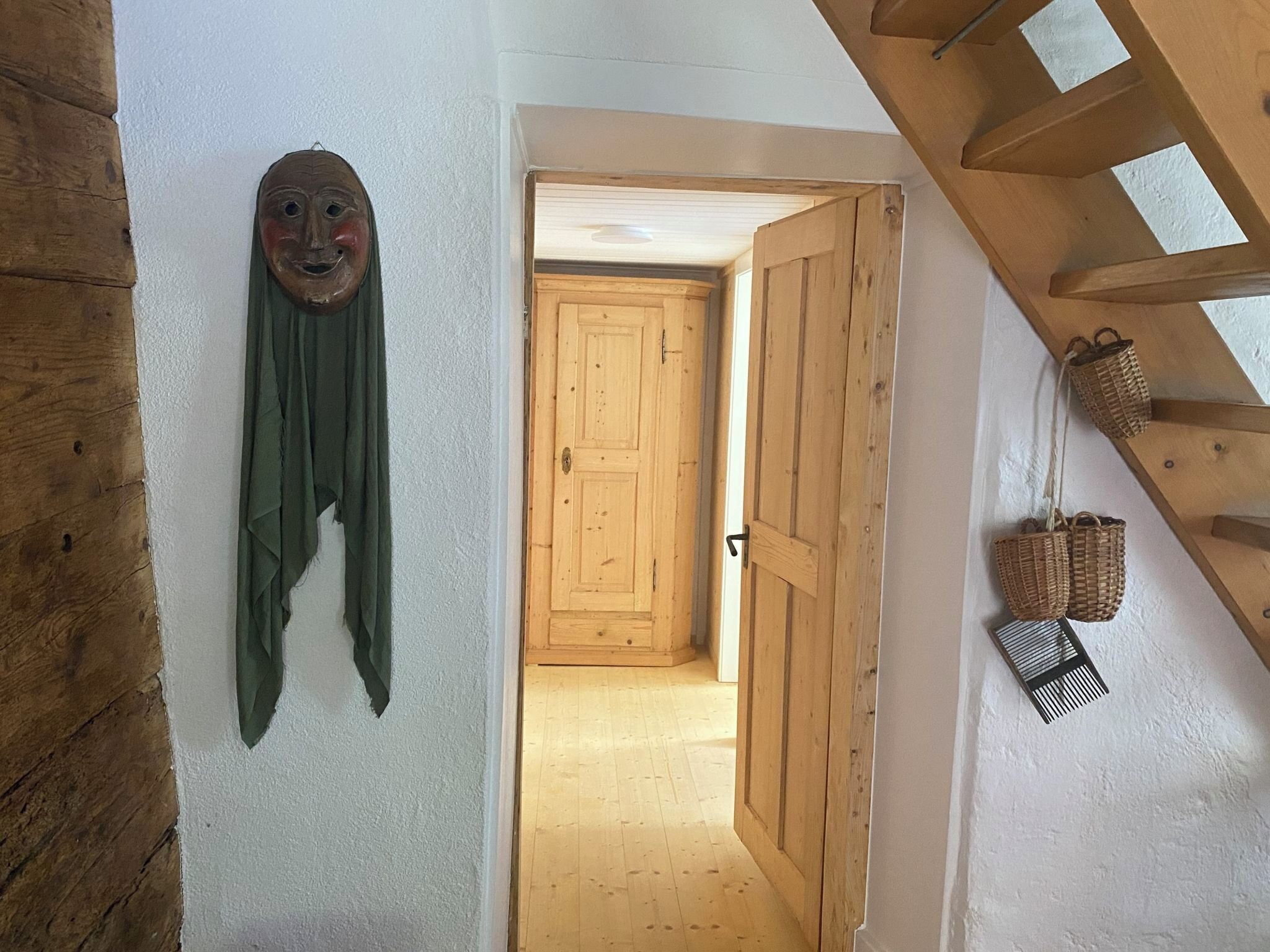 Une porte en bois qui donne sur un couloir doté d’un plafond en bois et d’un masque fixé au mur.