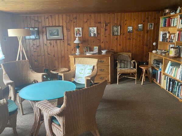 A room with a round table, wicker chairs, a bookshelf, and framed pictures on the wall.