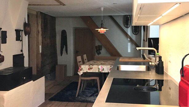 A compact kitchen with a built-in stove, a dining area with a table and chairs, and a staircase leading to another level. - Geelerhaus, (Berschis), by Interhome (Walenstadt)
