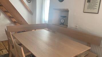 Ein Eckzimmer mit Holztisch und Bänken, einer Treppe und einer Wanduhr.