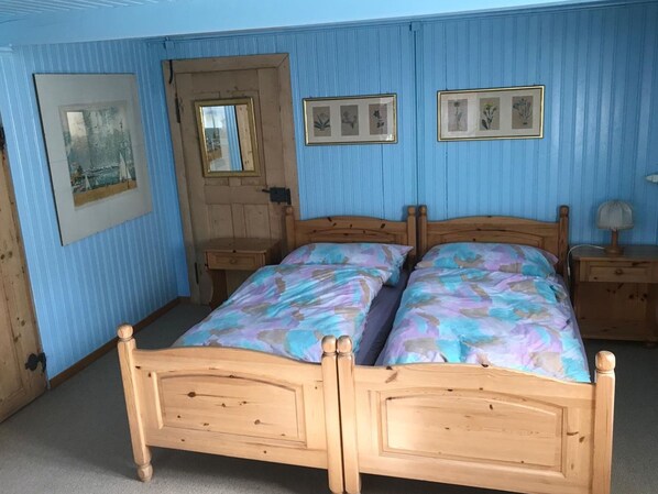 A bedroom with two wooden beds, a wooden wardrobe, a door with a mirror, and two framed pictures on the wall.