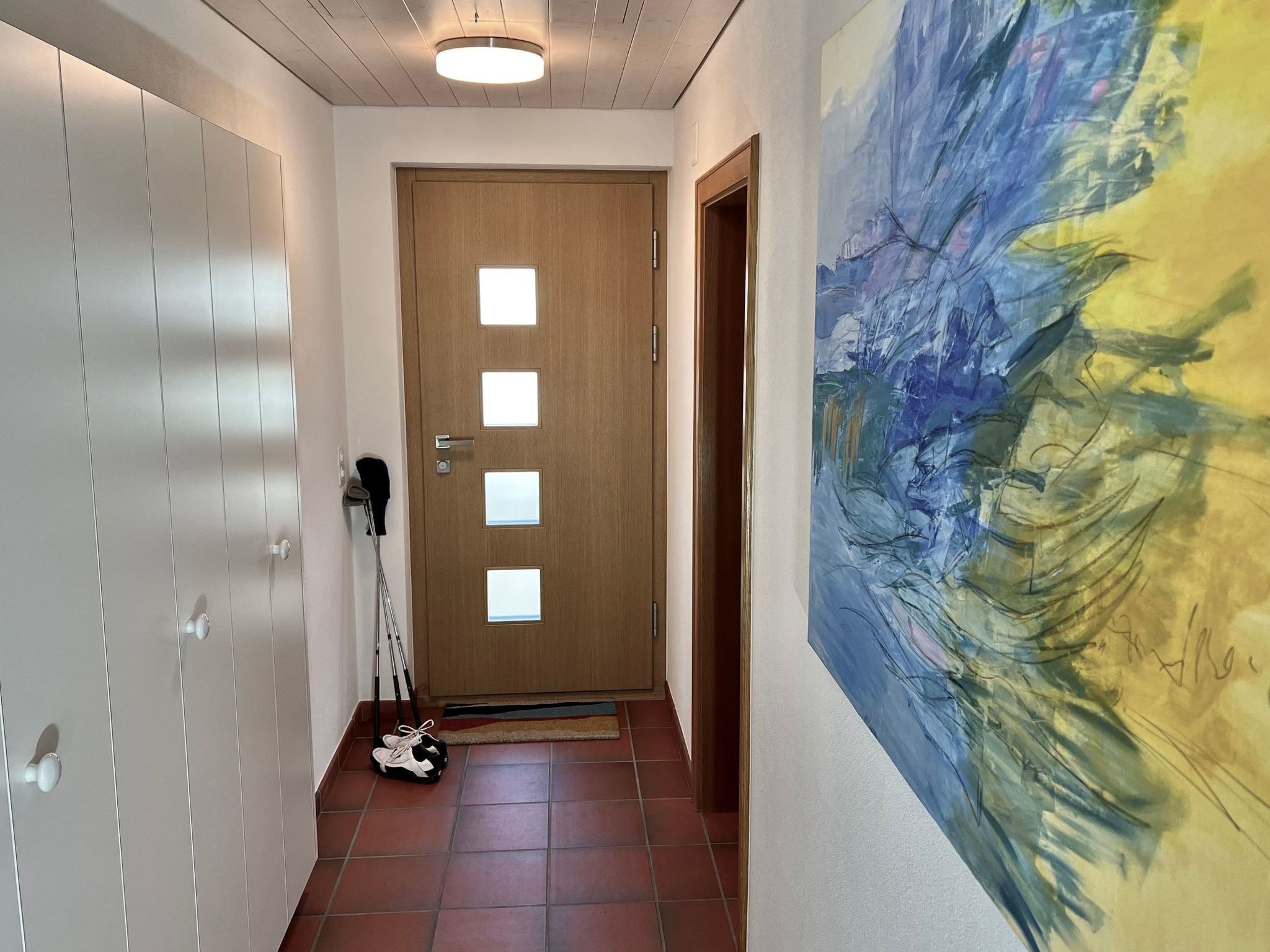 A hallway with a wooden door, a wheelchair, and a large abstract painting on the wall.