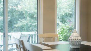 Ruokailutila, jossa on pöytä, tuoleja ja suuret ikkunat, joista avautuu näkymä vehreään maisemaan.