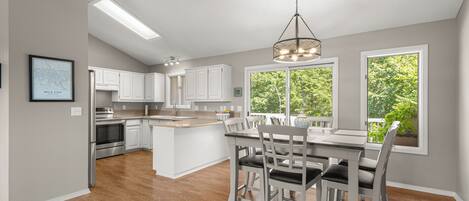 Una cocina moderna con armarios blancos, una isla central y una zona de comedor con mesa y sillas.