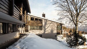 A snow-covered pathway leading to a building with a wooden facade and a view of mountains in the background. - Club Siesta Ferienwohnung/Studio, (Flumserberg Tannenheim), by Interhome (Flumserberg Tannenheim)
