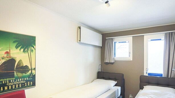 A hotel room with two single beds, a red chair, a poster on the wall, and a window with curtains. - Club Siesta Ferienwohnung/Studio, (Flumserberg Tannenheim), by Interhome (Flumserberg Tannenheim)